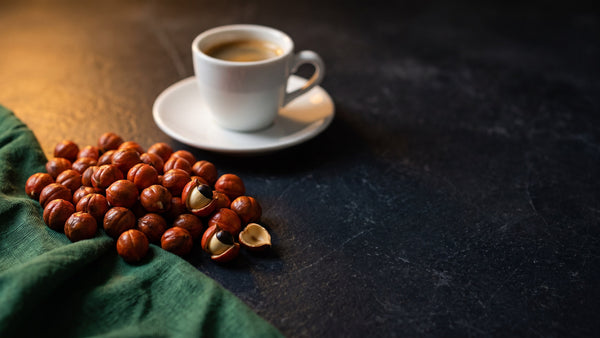 Roasted guarana seeds and a small espresso cup on dark slate under warm lamp light